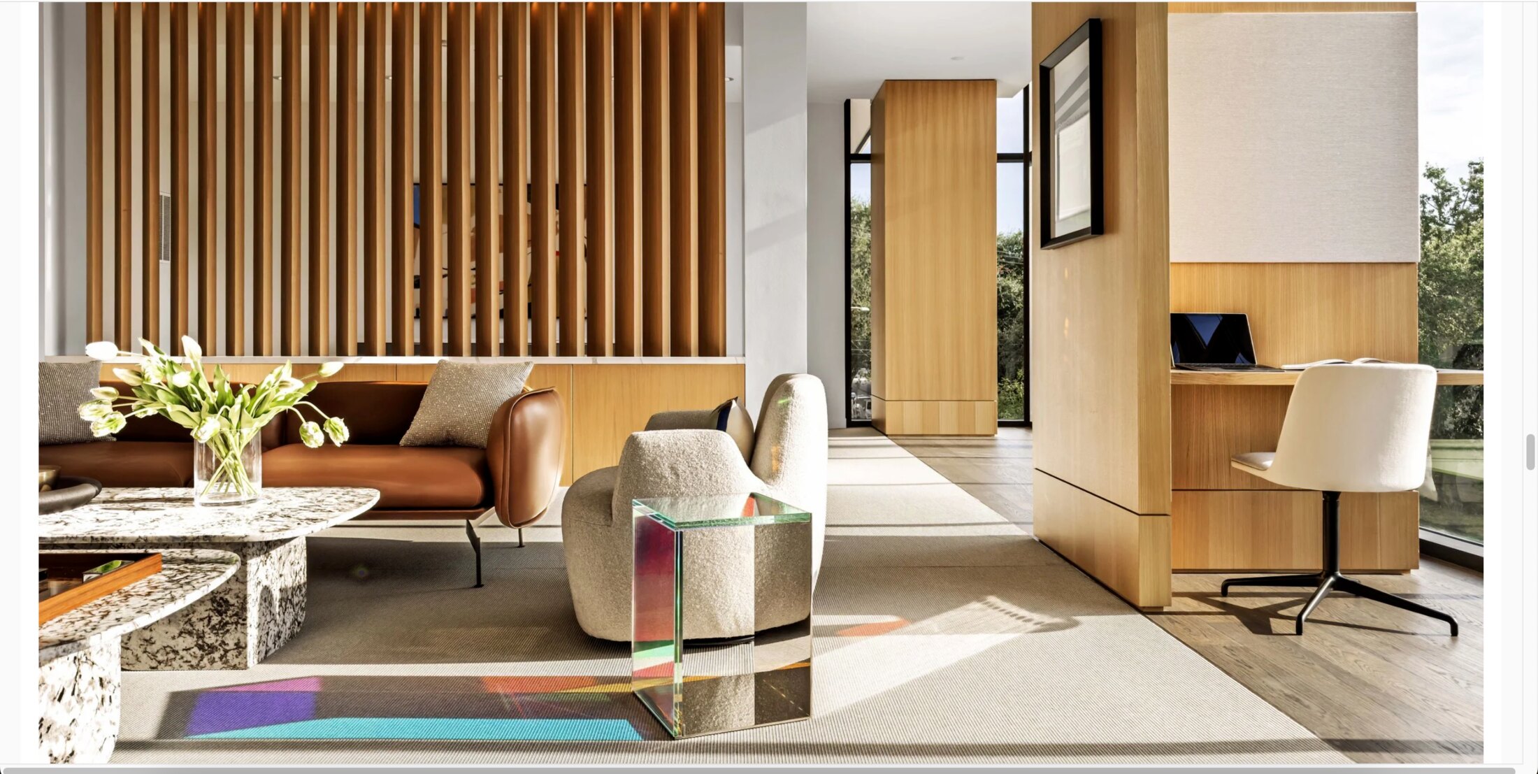 The Rone Residence living room by Rottet Studio — warm wood-slat wall, leather sofa, boucle armchairs, and a prismatic glass side table